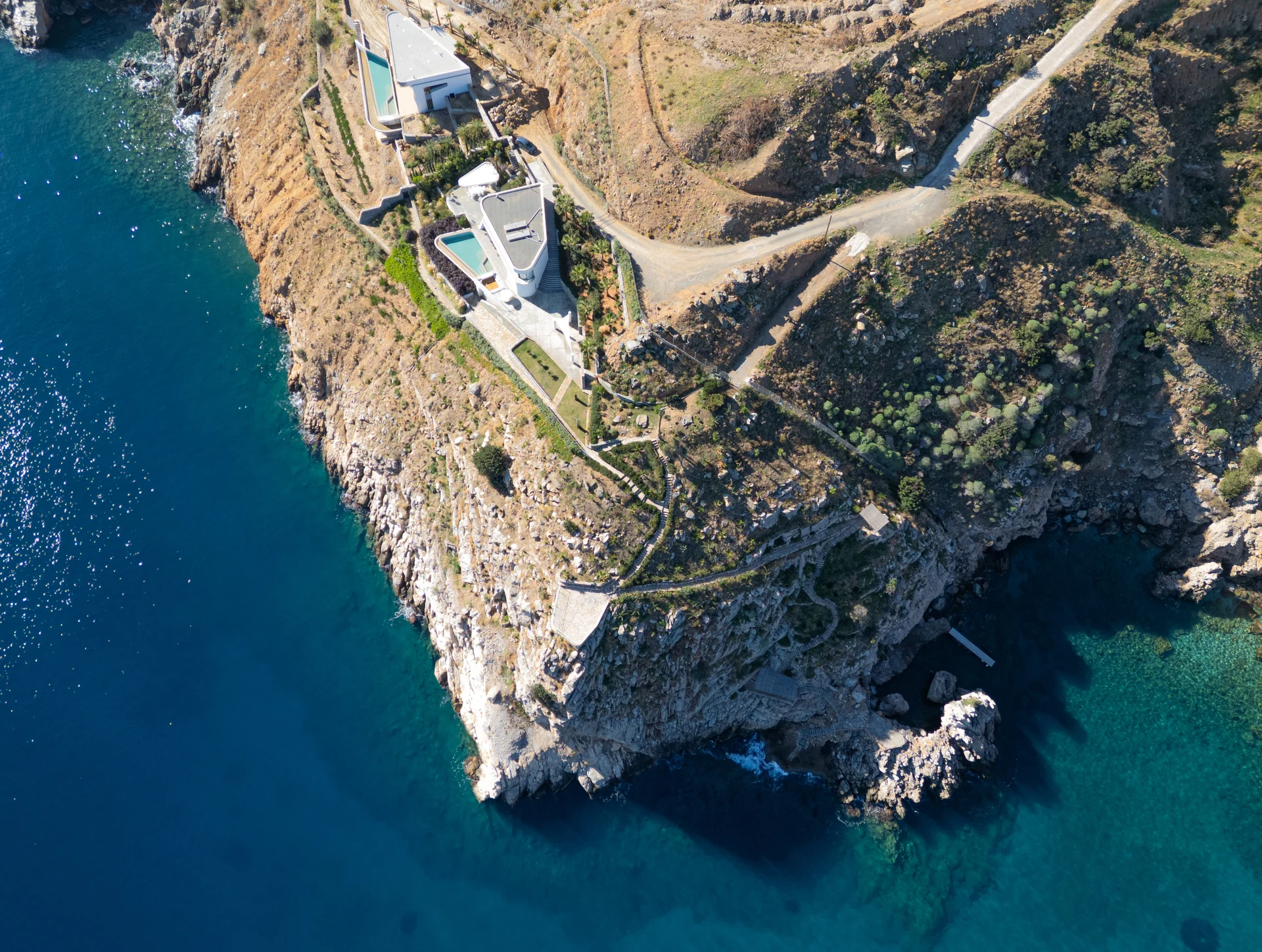 Aerial view of Meltemi Villa estate perched on cliff above the Aegean Sea, Heraklion Crete — full estate and private cove visible